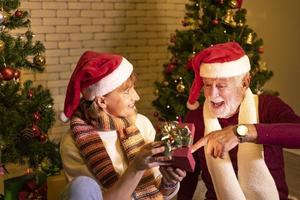 senior caucasian par fira jul tillsammans i lycka och spänning på Hem med röd santa hatt och jul träd foto
