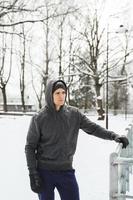 atletisk man bär luvtröja under hans vinter- träna i snöig stad parkera foto