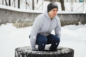 stark sportsman under hans crosstraining med en däck träna under snöig och kall vinter- dag. foto