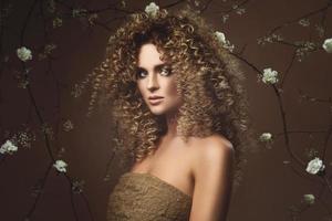 härlig ung kvinna med afro frisyr och skön smink med en massa av vit blommor foto