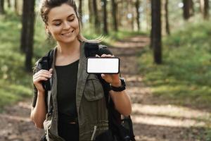 kvinna vandrare som visar smartphone med tom visa i grön skog foto