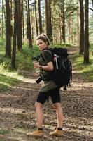 kvinna vandrare med stor ryggsäck och återanvändbar flaska för vatten i grön skog foto