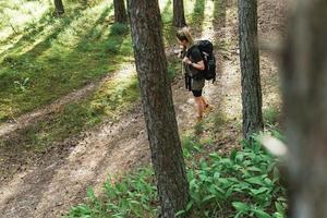 kvinna vandrare med stor ryggsäck i grön skog foto