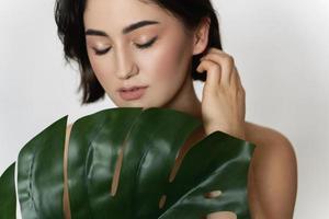 skön kvinna med en slät hud innehav grön tropisk blad på vit bakgrund foto