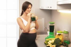 Lycklig gravid kvinna dricka friska grön smoothie foto