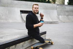 handikappade kille med en kopp av kaffe innan longboard ridning i en skatepark foto
