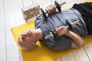 äldre man utövar med en hantlar under hans träna i Hem Gym foto