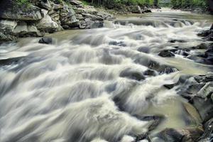 en berg flod långsamt flöden över de stenar tycka om en små vattenfall. foto