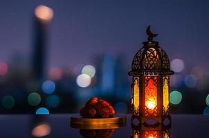 lykta den där ha måne symbol på topp och små tallrik av datum frukt med natt himmel och stad bokeh ljus bakgrund för de muslim fest av de helig månad av ramadan kareem. foto