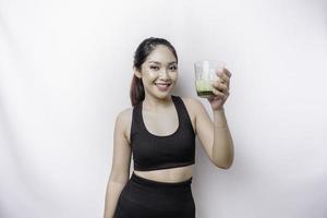 glad sportig asiatisk kvinna bär sportkläder med glas av gott grön smoothie, isolerat på vit bakgrund. foto