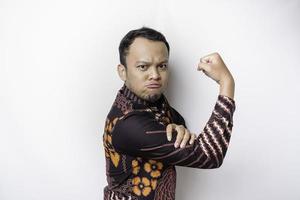 upphetsad asiatisk man bär batik skjorta som visar stark gest förbi lyft hans vapen och muskler leende stolt foto