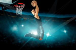 koncentrerad basketboll spelare i svart jersey gör omvänd slam dunka foto