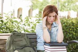 kvinna studerande utanför med huvudvärk Sammanträde med böcker och ryggsäck foto