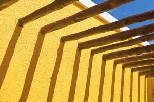 abstrakt trä posta balkar och ljus gul vägg mot blå himmel foto