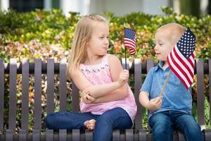 ung syster och bror jämförande varje andra amerikan flagga storlek på de bänk på de parkera foto