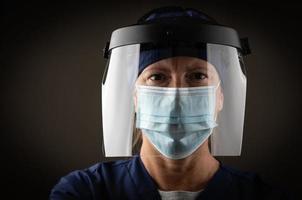 kvinna medicinsk arbetstagare bär skyddande ansikte mask och redskap mot mörk bakgrund foto