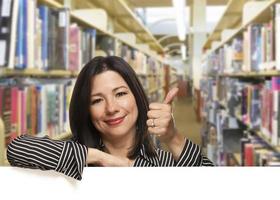 latinamerikan kvinna med tummen upp på vit styrelse i bibliotek foto