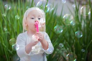 förtjusande liten flicka Sammanträde på bänk har roligt med blåser bubblor utanför. foto