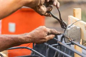 arbetstagare säkring stål armeringsjärn inramning med tråd plier fräs verktyg på konstruktion webbplats foto