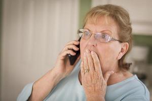 chockade senior vuxen kvinna på cell telefon i kök foto