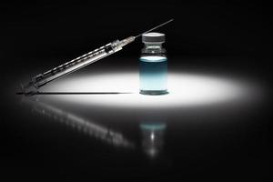 spruta nål och medicin injektionsflaska med ljus blå kemisk fläck belyst på reflekterande bakgrund foto
