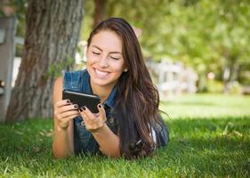 attraktiv Lycklig blandad lopp ung kvinna textning på henne cell telefon utanför om i de gräs foto