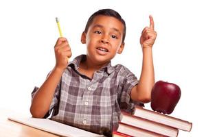 latinamerikan pojke höjning hans hand, böcker, äpple, penna och papper foto