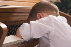 ung pojke med huvud på de piano foto