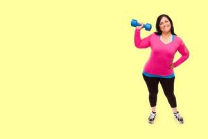 mitten åldrig latinamerikan kvinna i träna kläder innehav hantel mot en ljus gul bakgrund foto