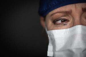 tårfylld betonade kvinna läkare eller sjuksköterska bär medicinsk ansikte mask på mörk bakgrund foto