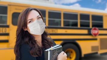 kvinna studerande nära skola buss bär medicinsk ansikte masker under coronavirus pandemi foto