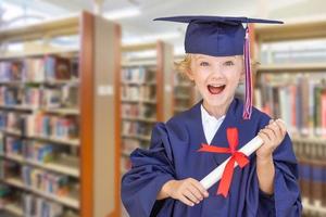 söt ung caucasian pojke bär gradering keps och klänning i de bibliotek foto