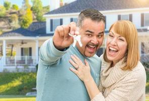 Lycklig blandad lopp par i främre av hus med ny nycklar foto