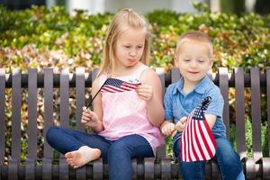 ung syster och bror jämförande varje andra amerikan flagga storlek på de bänk på de parkera foto