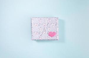 gåva låda insvept med grå papper med blommig mönster och rosa hjärta på ljus blå bakgrund. hjärtans dag. foto