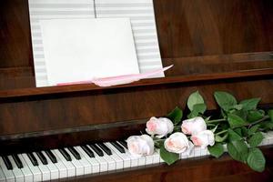 piano, bukett av fem blek rosa ro på tangentbord, musik papper foto