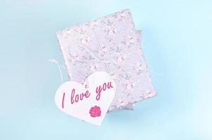 gåva lådor insvept med grå papper med blommig mönster och vit papper hjärta med ord jag kärlek du på ljus blå. foto
