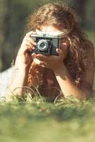 Söt hippie flicka på de gräs tar foton med ett gammal kamera - årgång effekt Foto