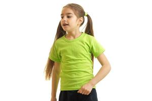 söt liten flicka i en grön t-shirt står i de studio och utseende mot foto