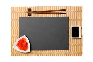 tömma rektangulär svart skiffer tallrik med ätpinnar för sushi, ingefära och soja sås på gul bambu matta bakgrund. topp se med kopia Plats för du design foto
