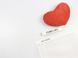 platt lägga av vana tracker bok, trä- kalender februari, röd hjärta form kudde på vit bakgrund med kopia Plats. foto