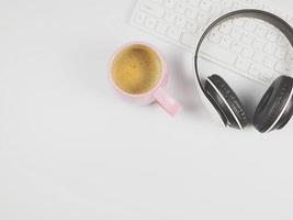 platt lägga av hörlurar på dator tangentbord och rosa kopp av kaffe på vit bakgrund. foto