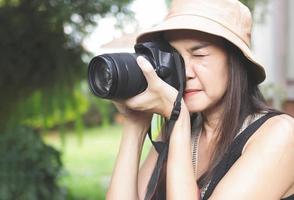 asiatisk kvinna bär hatt och ärmlös topp tar foton i de parkera med dslr kamera.