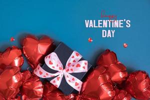 Lycklig valentines dag text och gåva låda med röd hjärta form baloons på blå bakgrund. valentines dag hälsning kort foto