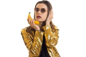 rolig eleganta flicka i gyllene jacka talande med banan tycka om en mobil telefon foto