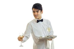 bra ung servitör utseende sidled ler och tar en glas av vin med en bricka foto