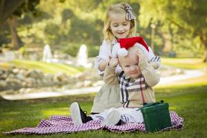 liten flicka försöker till sätta santa hatt på bebis bror foto