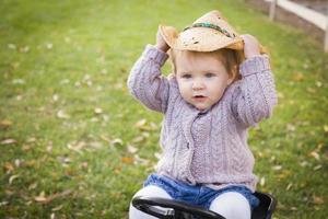 litet barn bär cowboy hatt och spelar på leksak traktor utanför foto