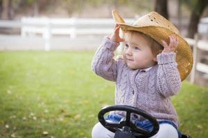 litet barn bär cowboy hatt och spelar på leksak traktor utanför foto