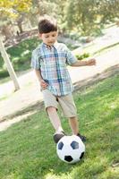 söt ung pojke som leker med fotboll utomhus i parken. foto
